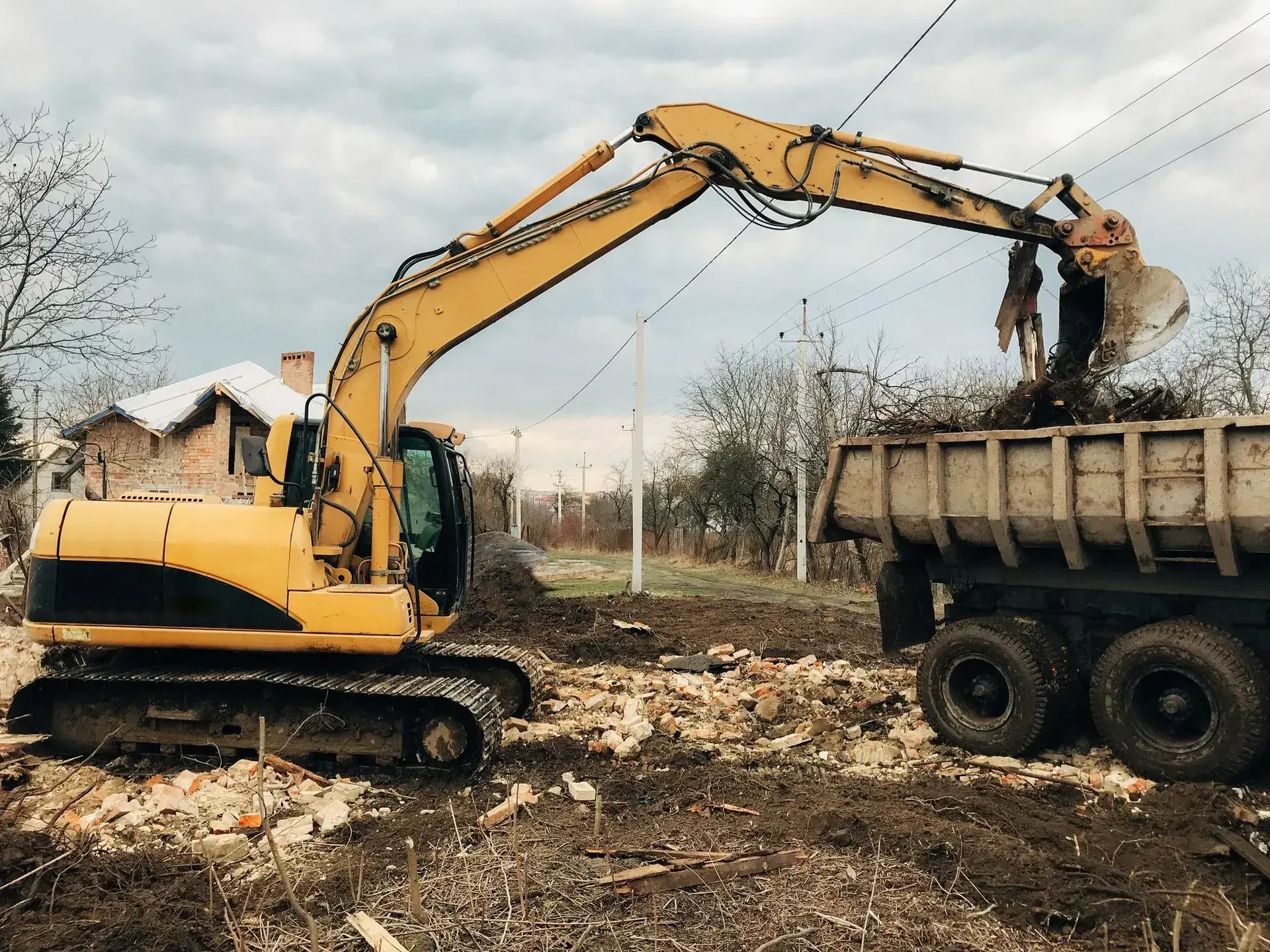Excavator loading cleared brush and debris into a dump truck on an open lot
