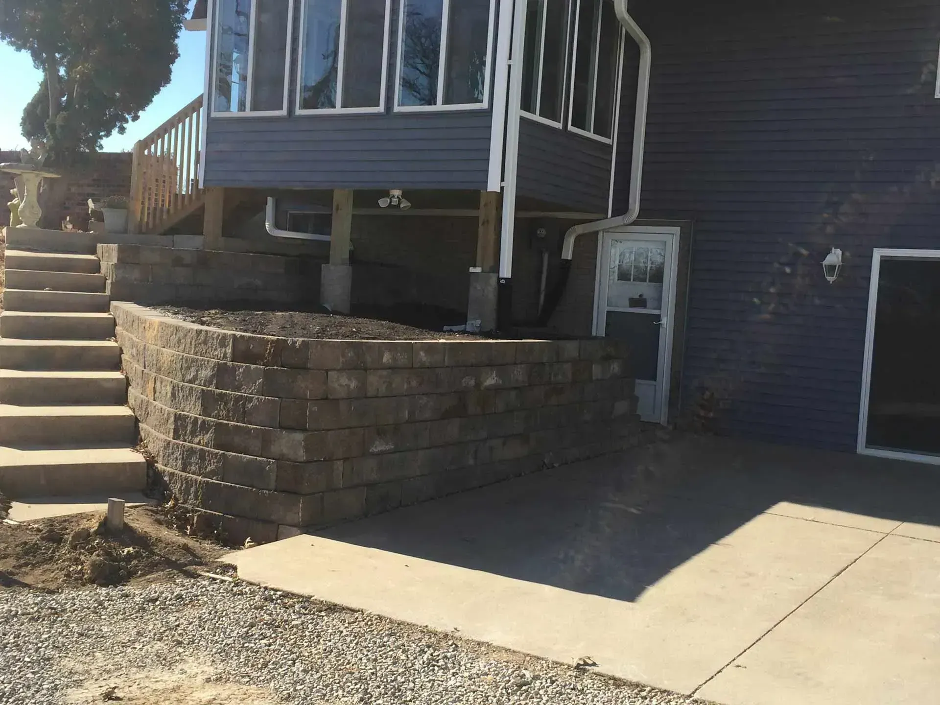 Stone retaining wall supports a deck with stairs and a house.