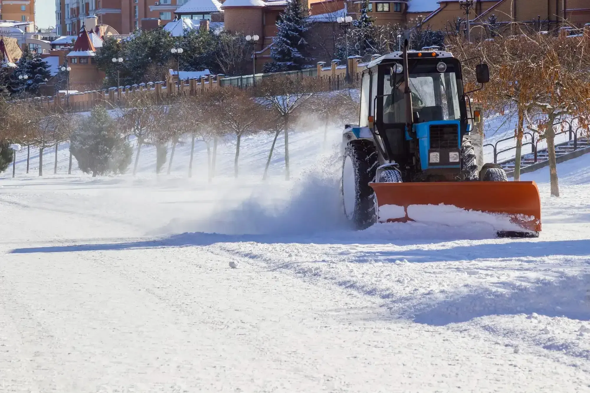 Tractor with an orange plow blade clearing snow from a road