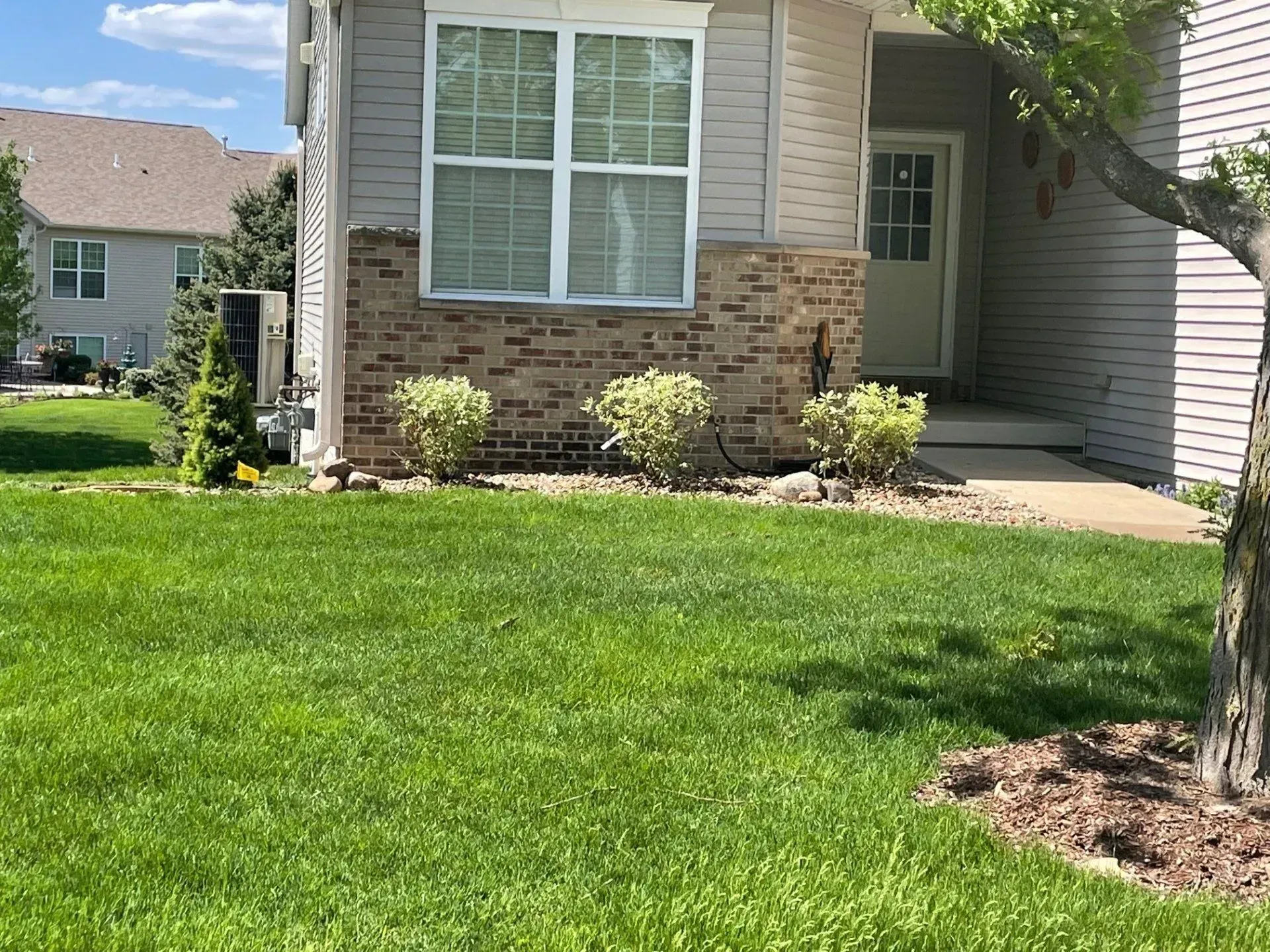 Exterior of a light-colored townhouse with green lawn and small shrubs. Brick accents on the facade.